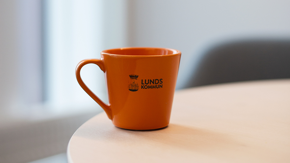 En bild på en orange kaffekopp där det står Lunds kommun